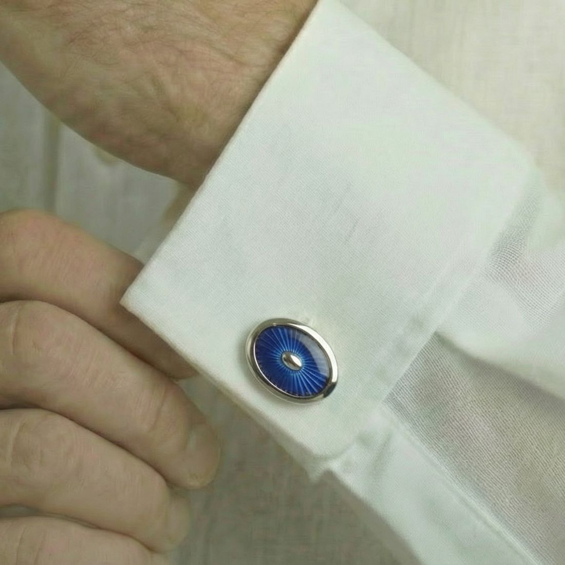 Close-up of a white shirt cuff with a blue and silver cufflink. Bown of London