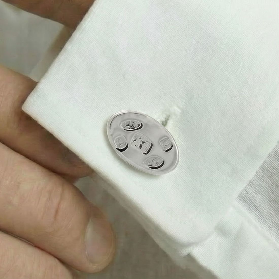 Close-up of a silver cufflink on a white shirt cuff. Bown of London.