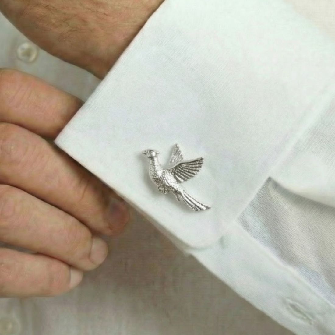 Silver bird-shaped cufflink on a white shirt cuff. Bown of London