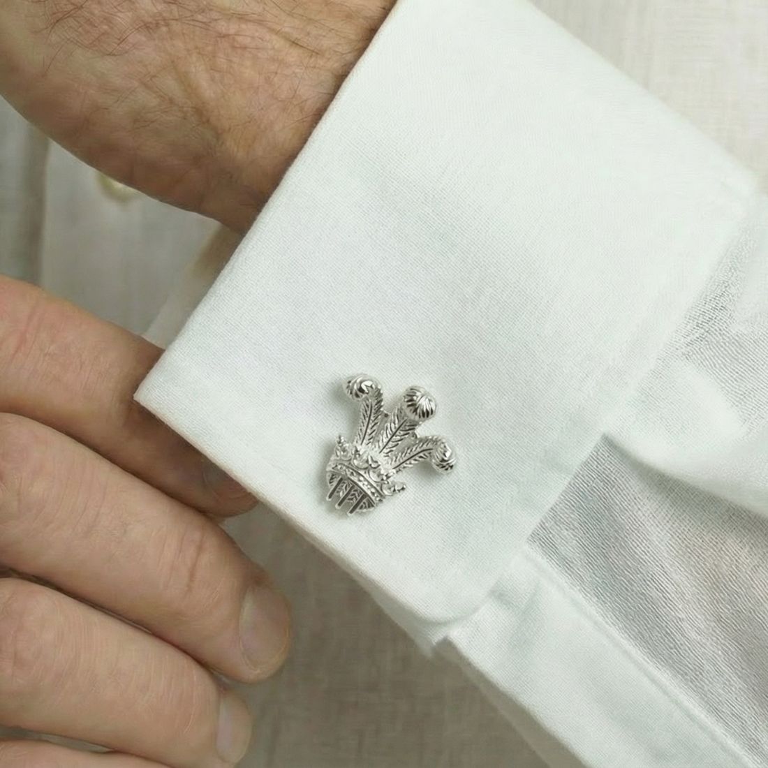 Silver crown-shaped cufflink on a white shirt cuff. Bown of London