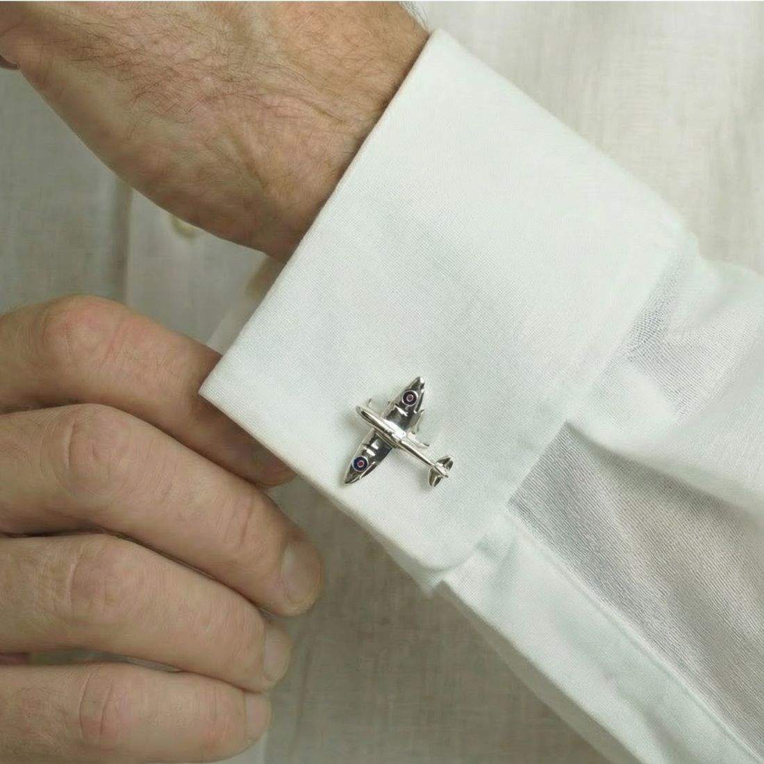 Cufflink shaped like a small airplane on a white shirt cuff.