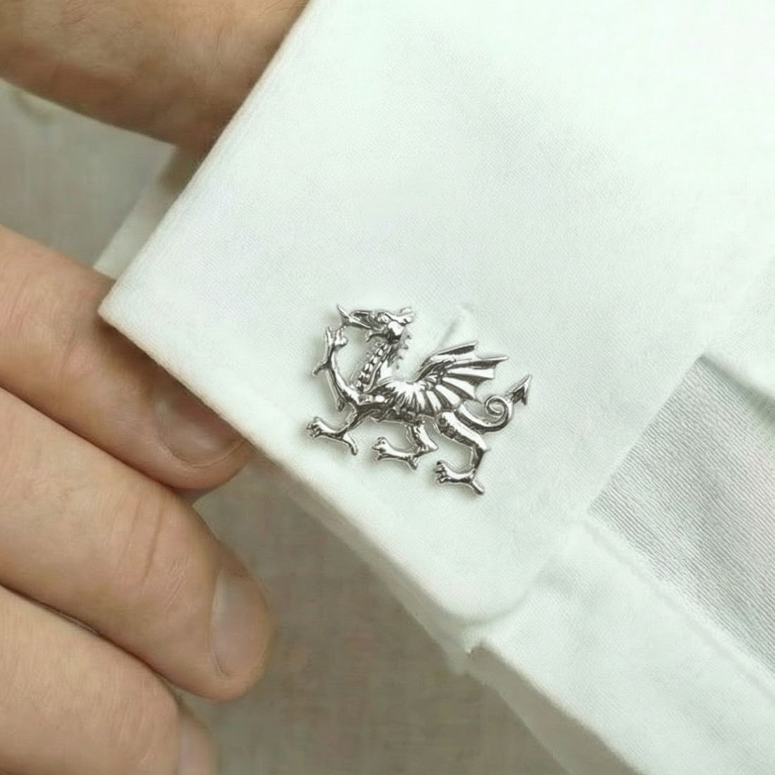 Silver dragon cufflink on a white shirt with a hand holding it. Bow of London