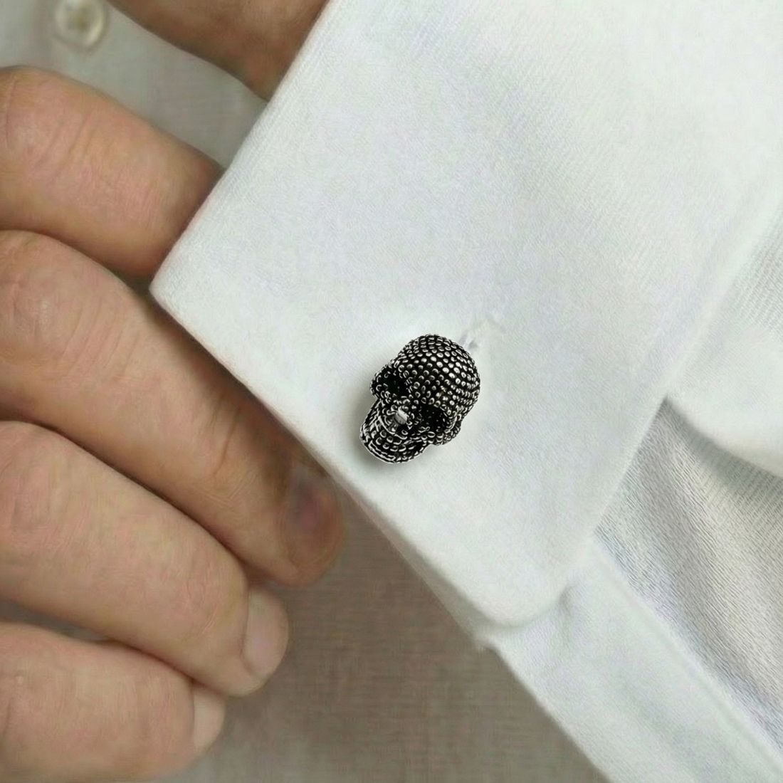 Close-up of a white shirt cuff with a black skull design button. Bown of London