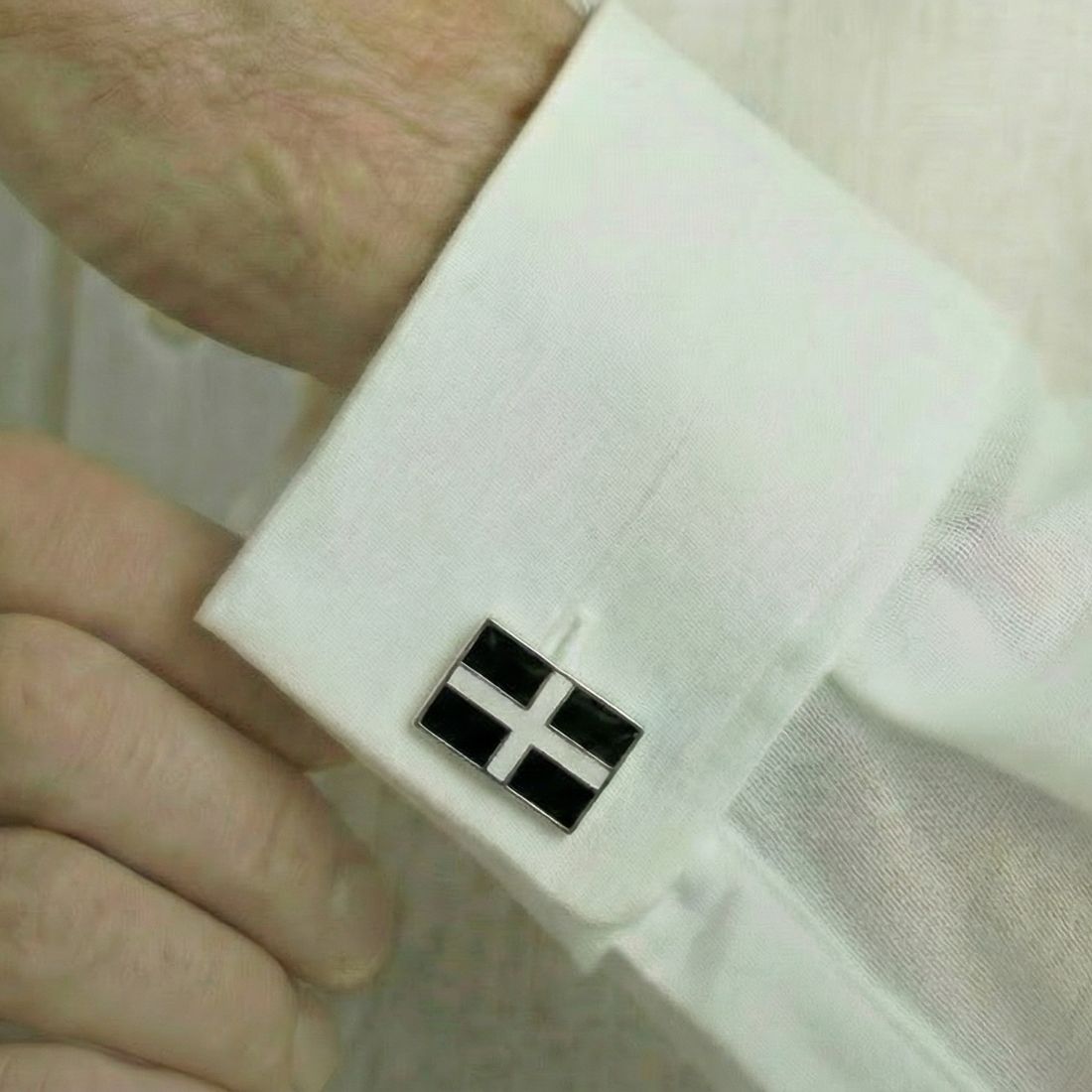 Cufflink on a white shirt with a hand adjusting it. Bown of London
